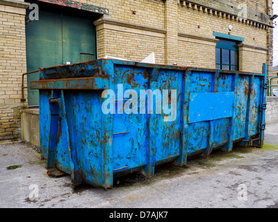 Un arrugginito, rifiuti blu saltare in piedi di fronte ad un edificio in mattoni. Foto Stock