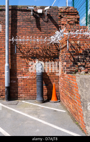 Un'immagine per illustrare le misure di sicurezza - telecamere TVCC, catena-link recinzioni e un anti-salita, aggeggio di metallo fissata ad una parete. Foto Stock