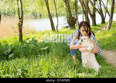 Attraente casual donna giovane la piegatura verso il basso e coccole il suo piccolo cane come essi una passeggiata anche se la pacifica rigogliosa campagna Foto Stock