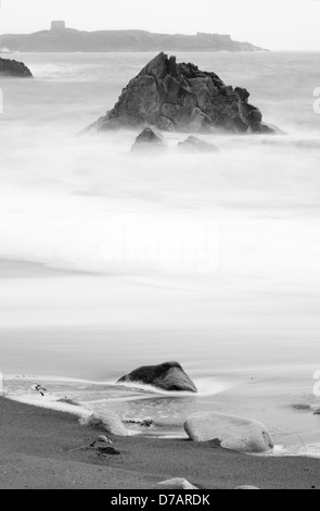 Una lunga esposizione colpo di onde che lambiscono su una spiaggia rocciosa. Foto Stock