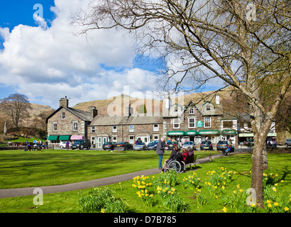 La gente seduta sulle panchine intorno al villaggio verde godendo il sole primaverile in Grasmere Cumbria Inghilterra UK GB EU Europe Foto Stock