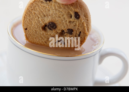 Persona britannica dunking un cioccolato biscotto di chip in una tazza di tè e caffè in porcellana bianca tazzina per tea break. Inghilterra, Regno Unito, Gran Bretagna Foto Stock