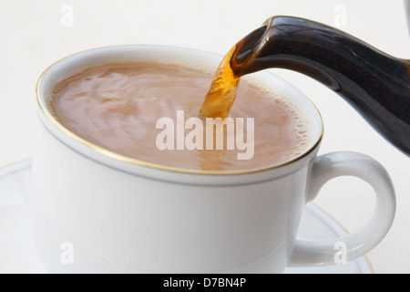 Preparazione versare una tradizionale tazza inglese di tè da un beccuccio di teiera in un teacup cinese bianco con latte messo in primo luogo. Inghilterra Gran Bretagna Foto Stock