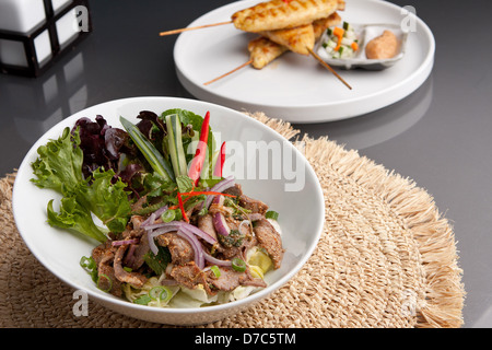 Stile asiatico insalata Thai con manzo e pollo satay di pollo alla brace su spiedini antipasti in background. Foto Stock