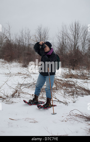 Una donna fotografo è fuori riprese su racchette da neve su una giornata invernale nel Berkshires, Massachusetts. Foto Stock