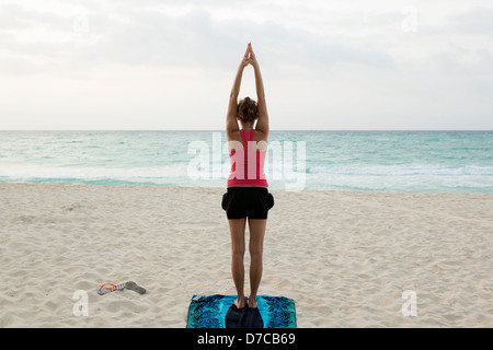 Messico, Playa del Carmen, giovane donna a praticare yoga sulla spiaggia al sorgere del sole Foto Stock