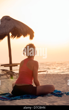 Messico, Playa del Carmen, giovane donna a praticare yoga sulla spiaggia al sorgere del sole Foto Stock