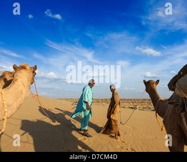Rajasthan travel background - due indiani cameleers (camel driver) con i cammelli in dune del deserto di Thar. Jaisalmer, Rajasthan Foto Stock