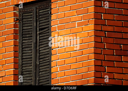 Muro di casa in mattoni con finestre chiuse con sfumature di legno. Foto Stock