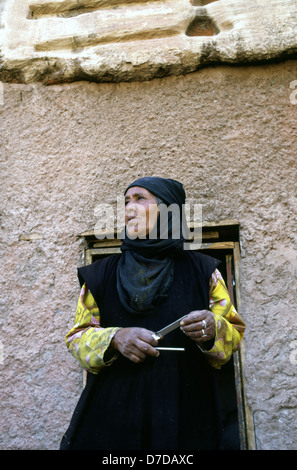 Un'anziana donna beduina dalla tribù Bedul Uno della tribù Huwaitat che storicamente hanno vissuto in Petra indossando abiti tradizionali sorge all'entrata di una caverna residence tagliata nella roccia di Wadi Musa vicino a Petra Giordania Foto Stock