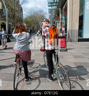 Coppia giovane dietro visualizza stop vicino a negozi di biciclette durante il ciclismo in Cardiff City Centre a St. David's 2 shopping street zona Wales UK KATHY DEWITT Foto Stock