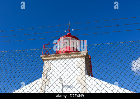 Faro luminoso al di là di catena collegamento recinto contro il cielo blu sullo sfondo Foto Stock