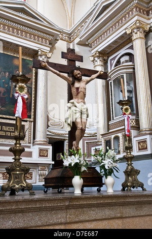 Statua policroma della crocifissione Martire di Cristo sulla croce di legno con la Pasqua fiori & rosette chiesa della Compagnia di Gesù Foto Stock