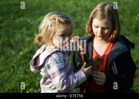 Due bambini bionda ragazze giocare con giardino di erba e fiori in estate Foto Stock