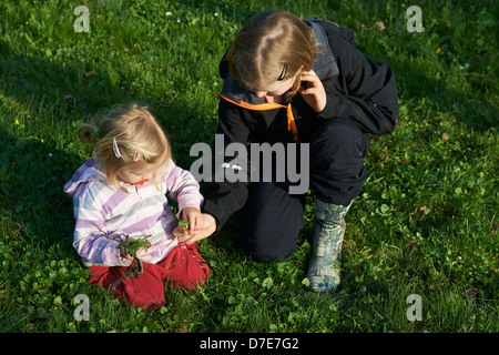Due bambini bionda ragazze giocare con giardino di erba e fiori in estate Foto Stock