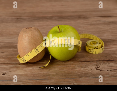 Concetto di dieta, kiwi con mela verde e nastro di misurazione su uno sfondo di legno Foto Stock