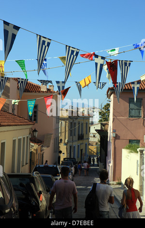 Persone passeggiando per le stradine del quartiere Plaka di Atene con le bandiere Greca infilate tra gli edifici Foto Stock