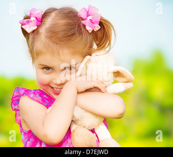 Sorridenti ragazza con bel giocattolo morbido nel giardino Garderie, avendo divertimento all'aperto, stagione primaverile, infanzia felice concetto Foto Stock