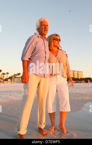 A piedi nudi coppia senior passeggiando lungo la spiaggia godendosi il tramonto Foto Stock