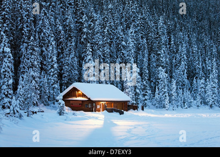 Una coperta di neve log cabin su una coperta di neve a lago circondato da alberi sempreverdi al crepuscolo;Lake Louise Alberta Canada Foto Stock