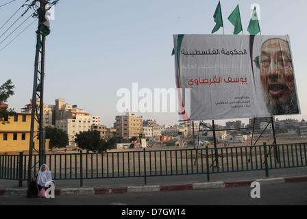 Luglio 31, 2012 - Gaza City, nella Striscia di Gaza, Territori palestinesi - Una donna Palestinese si siede accanto a un banner con immagine di eminente studioso Musulmano lo sceicco Yusuf al-Qaradawi, nella Striscia di Gaza City il 7 maggio 2013. Al-Qaradawi, Qatar-basato chierico che è largamente rispettata attraverso il mondo musulmano, e sottolinea il suo sostegno per il gruppo islamico di Hamas, sarà a capo di una delegazione di studiosi di domani nella sua prima visita alla striscia di Gaza (credito Immagine: © Naaman Omar/immagini APA/ZUMAPRESS.com) Foto Stock