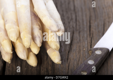Asparagi bianchi è con le punte in avanti su una tavola di legno accanto a un vecchio coltello con manico in legno Foto Stock