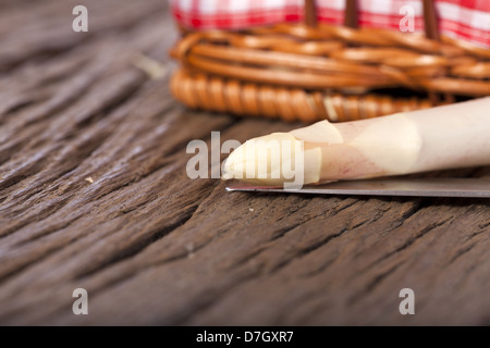 Ripresa macro di una punta di asparagi con un coltello su un rustico sfondo di legno fuori fuoco sullo sfondo di un piccolo carrello Foto Stock