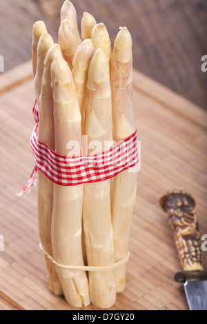 Bundle fresco di asparagi bianchi è su un tagliere in background al di fuori della messa a fuoco di un coltello con impugnatura in corno di bue Foto Stock