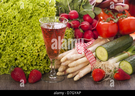 Ortaggi freschi con asparagi e strawbeeries su uno sfondo di legno e un bicchiere di vino rosato Foto Stock