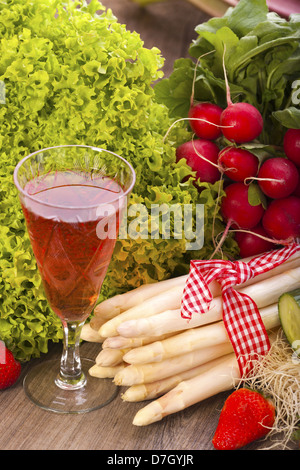Ortaggi freschi con asparagi e ravanelli su uno sfondo di legno e un bicchiere di vino rosato Foto Stock