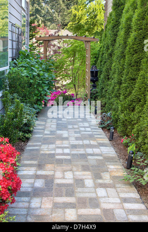 Giardino mattone lastricatore Percorso pedonale con legno Arbor luce del paesaggio di alberi e piante da fiore Foto Stock