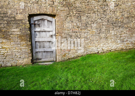 Vecchia porta di legno in una pietra alto muro del giardino Foto Stock