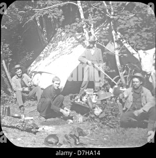 Una fotografia della Herman Bohlman Collection presso l'OSU Archives, che mostra le persone in campeggio in un ambiente all'aperto, con attività come la manipolazione dei fucili e la configurazione delle tende. La scena cattura gli aspetti pratici e di svago del campeggio a metà del XX secolo. Foto Stock
