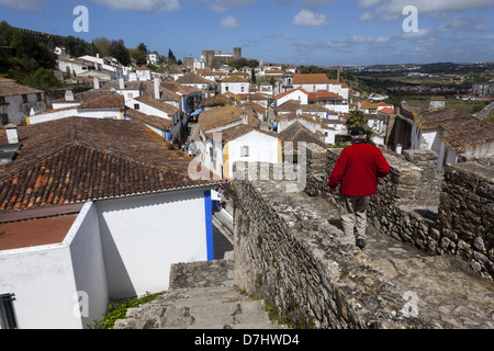 La collina del borgo medievale di Óbidos mostra un uomo a camminare sulle sue mura fortificate Foto Stock