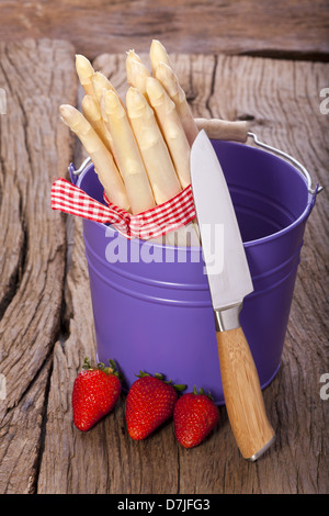 Asparagi freschi in un colorato cestelli metallici prima di un coltello e tre fragole Foto Stock