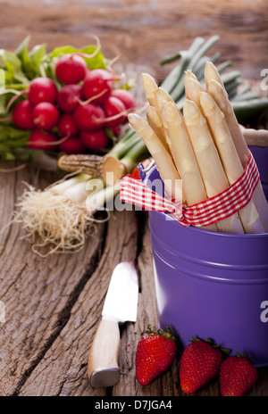 Asparagi freschi in un colorato cestelli metallici prima di un coltello e tre fragole Foto Stock