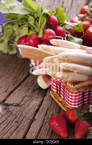 Asparagi freschi con un coltello in una cesta davanti a un paio di fragole in background un altro di verdura e di frutta Foto Stock