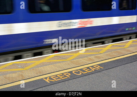 Un rapido movimento del treno stazione passando il bordo della piattaforma con mantenere chiara segnaletica di avvertimento antiscivolo per pavimentazioni e linea gialla la schiusa Foto Stock