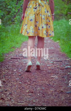 Le gambe di una donna in un abito giallo a piedi su un percorso nel bosco Foto Stock