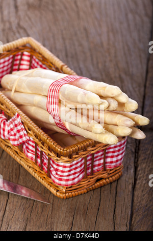 Asparagi bianchi legate con un nastro di tessuto in una cesta e un coltello Foto Stock