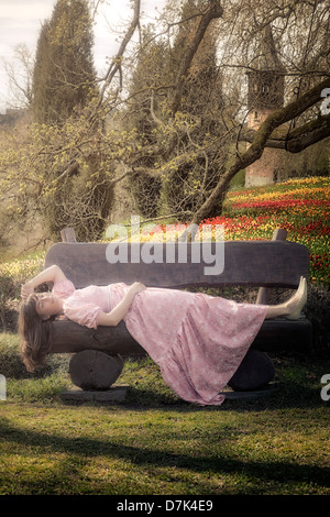 Una ragazza in un abito floreale è sdraiato su un banco in un parc Foto Stock