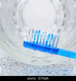 Un spazzolino da denti blu posa su un bagno umido contatore con un vetro sul suo lato in background. Foto Stock