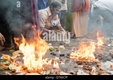 Un indù devoto interruzioni aperta una noce di cocco che offre nel mezzo di canfora di incendi. Arunachaleswara Tempio Tiruvannamalai, Tamil Nadu, India Foto Stock