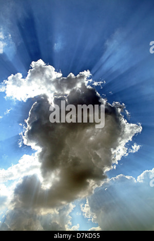 Raggi di sole lo scoppio attraverso e attorno a una nuvola in cielo Foto Stock