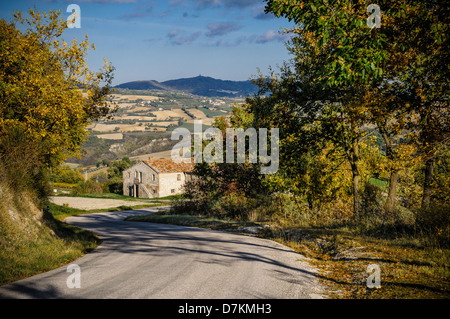 La guida in discesa su una piccola strada vicino a Urbino in Italia. Un antica casa onu viene visualizzata una curva. Foto Stock