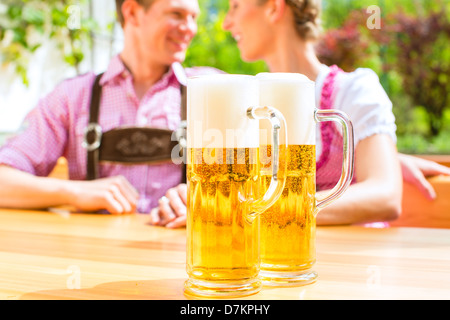 Felice coppia seduta nel giardino della birra in estate e gustare un bicchiere di birra e il sole, in permanente voreground due bicchieri Foto Stock