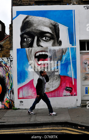 Un uomo cammina davanti ad una parete ricoperta di graffiti a Brick Lane, London, Regno Unito Foto Stock