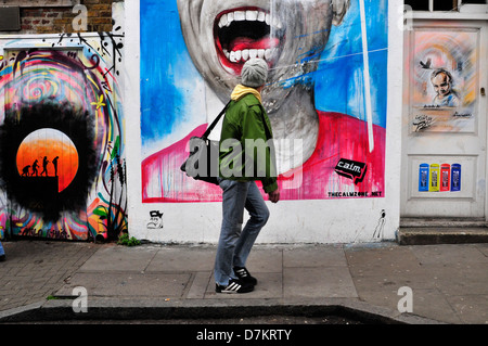 Un uomo guarda a graffiti a Brick Lane, London, Regno Unito Foto Stock