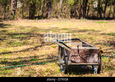 Un giardino carrello e strumenti con guanti hanging off il lato in quanto si trova in un prato pronto per andare al lavoro. Foto Stock