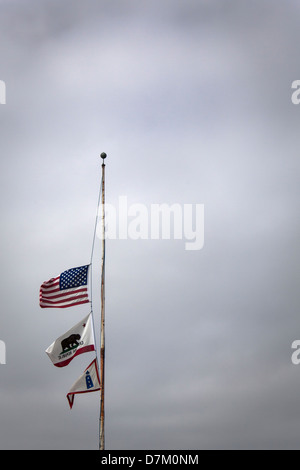 Gli Stati Uniti, per lo Stato della California e del faro Service bandiere volare a metà il montante o la metà del personale contro un grigio cielo nuvoloso. Foto Stock